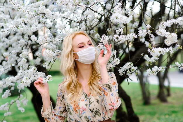 Młoda kobieta w ochronnej sterylnej masce medycznej na twarzy w wiosennym ogrodzie.