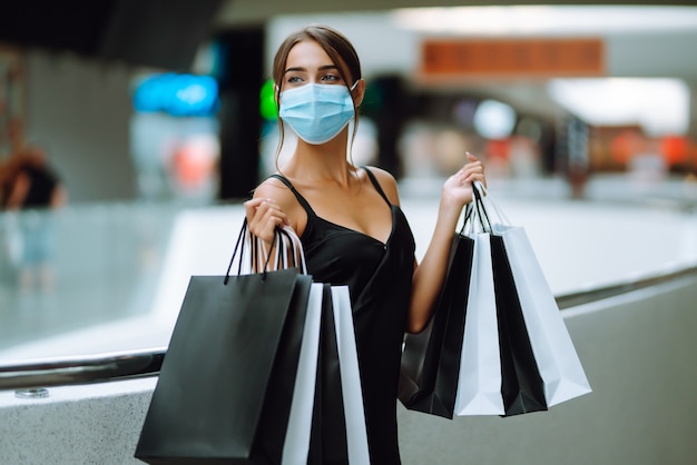 Młoda kobieta w ochronnej sterylnej masce medycznej na twarzy z torby na zakupy w centrum handlowym.