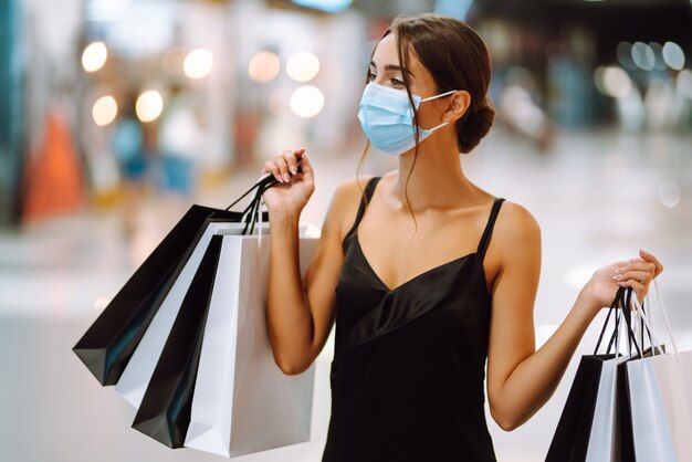 Młoda kobieta w ochronnej sterylnej masce medycznej na twarzy z torby na zakupy w centrum handlowym.