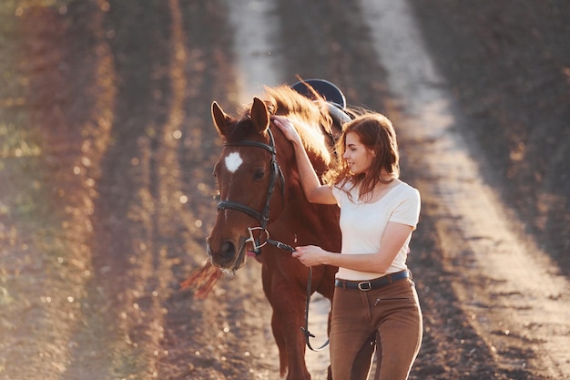 Młoda kobieta w ochronnym kapeluszu spacerująca z koniem w polu rolnictwa w słoneczny dzień