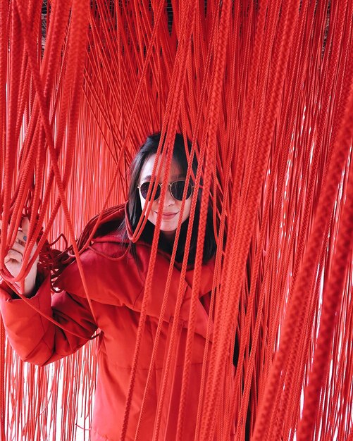 Młoda kobieta w okularach przeciwsłonecznych i czerwonym płaszczu ukrywająca się w czerwonych liniach