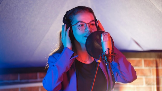 Młoda kobieta w okularach śpiewa w neonowym oświetleniu w studio