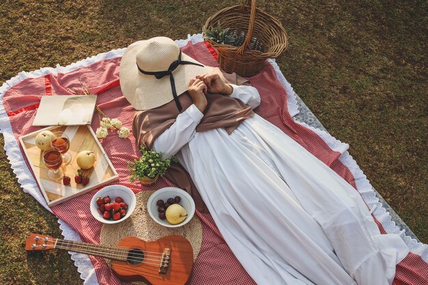 Zdjęcie młoda kobieta w parku drzemie na kocu piknikowym zakrywającym twarz słomkowym kapeluszem na su
