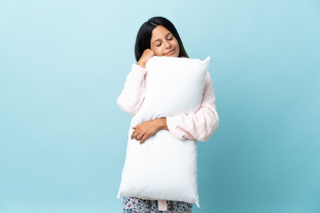 Młoda kobieta w piżamie na białym tle w piżamie i trzymając poduszkę podczas snu