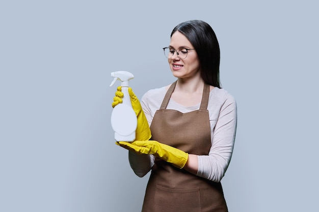 Młoda kobieta w rękawiczkach z detergentem organicznym na szarym tle