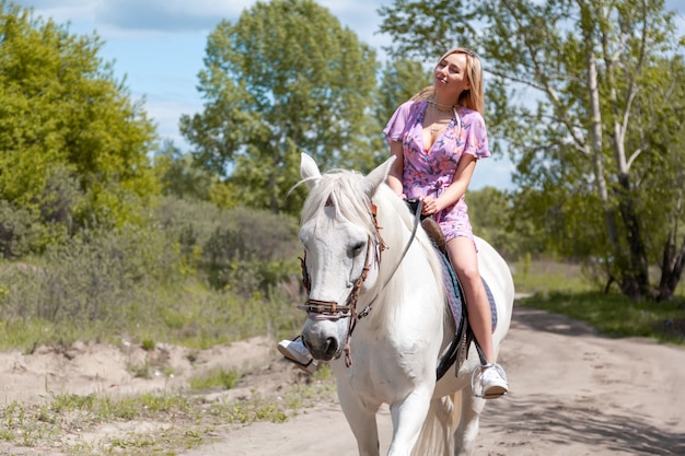 Młoda kobieta w romantycznej sukni z białym koniem w świetle zachodu słońca wieczorem. Fotografia plenerowa z dziewczyną modelki.