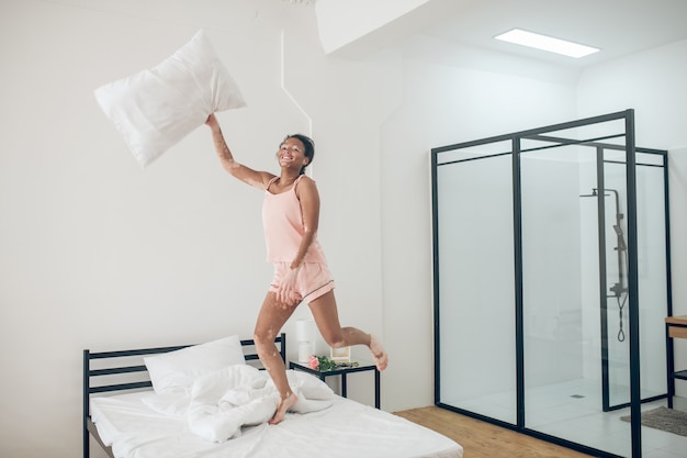 Młoda kobieta w różowej bieliźnie skacze na łóżku