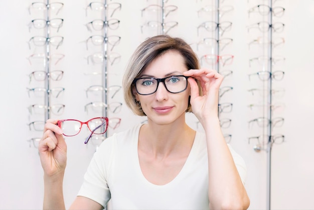 Młoda kobieta w sklepie optycznym wybiera nowe okulary z optykiem. okulary w sklepie optycznym. Kobieta wybiera okulary. Emocje. Okulistyka.