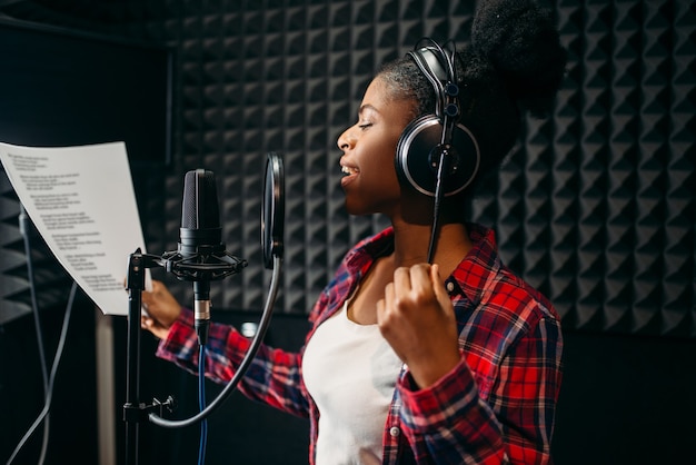 Młoda kobieta w słuchawkach piosenki w studio nagrań audio.