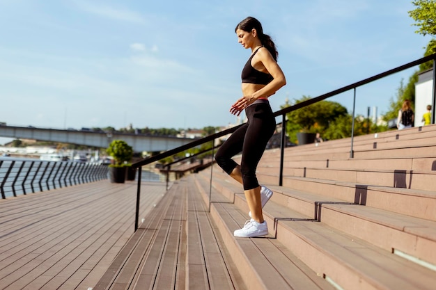 Młoda kobieta w sportowej ćwiczeniu na nadrzecznej promenadzie