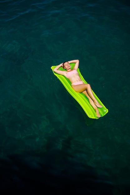 Młoda kobieta w stroju kąpielowym pływa na nadmuchiwanym jasnym materacu w morzu. Koncepcja wakacji letnich.
