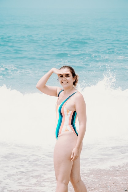 Młoda kobieta w stroju kąpielowym przed oceanem, odwracająca się do kamery i uśmiechająca się, kopiująca przestrzeń, wolność i koncepcja przyszłości