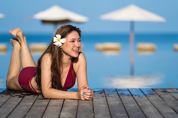 Młoda kobieta w stroju kąpielowym relaksuje się na drewnianej krawędzi basenu z morskim tłem
