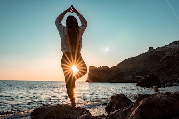 Młoda kobieta w stroju kąpielowym z długimi włosami ćwiczy rozciąganie na świeżym powietrzu na macie do jogi nad morzem w słoneczny dzień Kobieta jogi fitness pilates rutyna Zdrowy styl życia koncepcja harmonii i medytacji