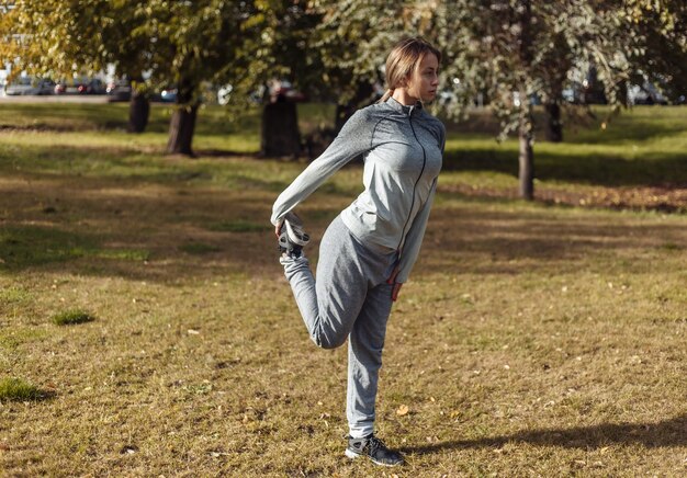 Młoda kobieta w stroju sportowym rozgrzewa się w parku jesienią