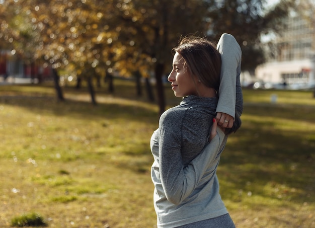 Młoda kobieta w stroju sportowym rozgrzewa się w parku jesienią