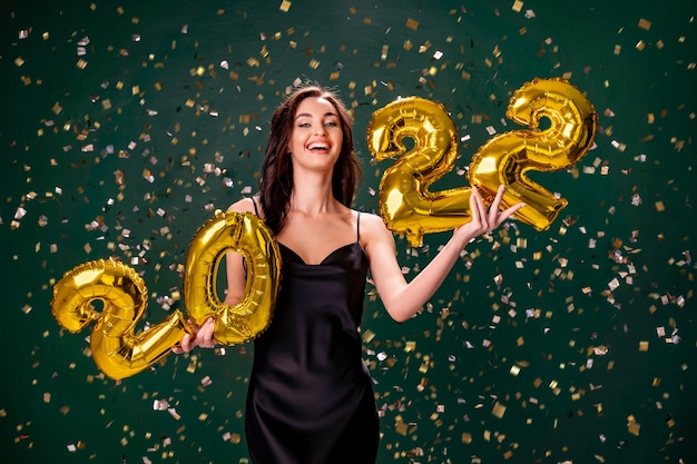Młoda kobieta w sukni koktajlowej świętująca nowy rok i trzymająca złote balony