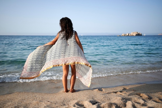Młoda kobieta w sukni na spokojnej plaży podziwiając horyzont nad wodą