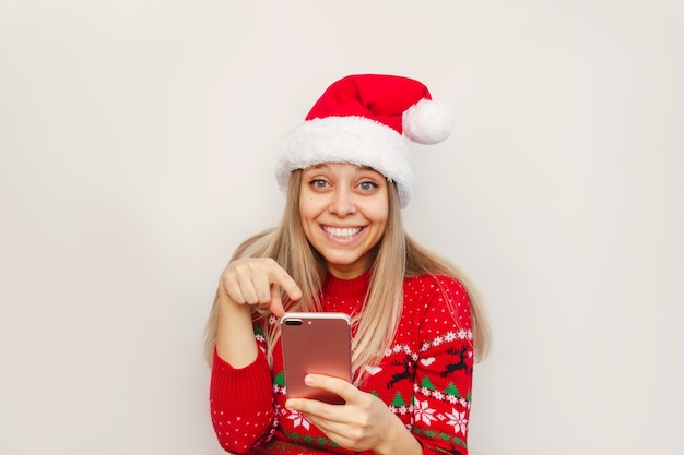 Młoda Kobieta W Sweterku Z Jelenia W Kolorze Czerwonym Kapelusz świętego Mikołaja Wskazuje Palcem Na Ekran Telefonu Komórkowego