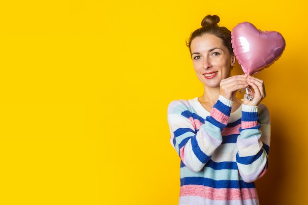 Młoda Kobieta W Swetrze Trzyma Serce Balonu Na żółtym Tle. Kompozycja Walentynkowa.