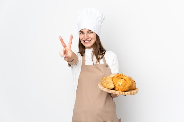 Młoda kobieta w szefa kuchni mundurze na białym uśmiechniętym i pokazuje zwycięstwo znaku