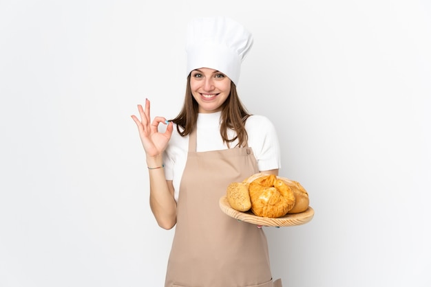 Młoda kobieta w szefa kuchni mundurze na biel ścianie pokazuje ok znaka z palcami