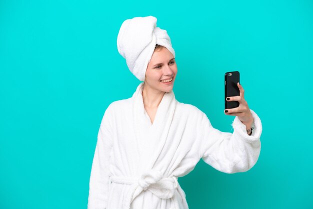 Młoda kobieta w szlafroku na białym tle na niebieskim tle robi selfie