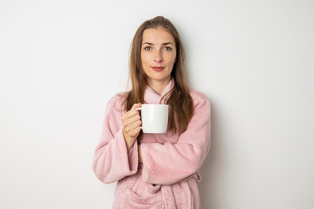 Młoda kobieta w szlafroku pije kawę na białym tle