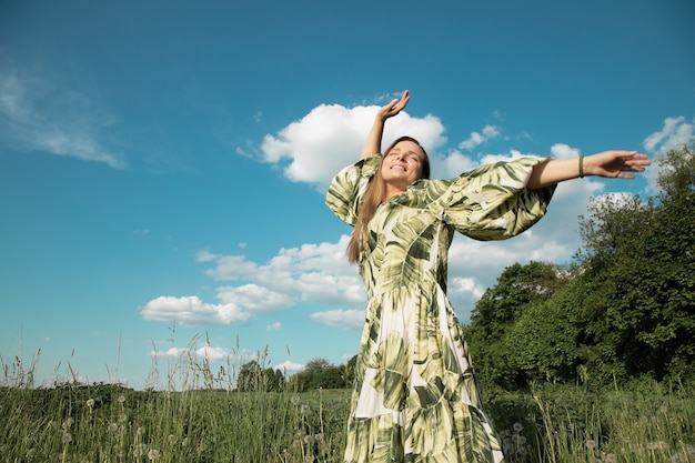 Młoda kobieta w zielonym polu z rękami wyciągniętymi w kierunku błękitnego nieba, szczęście