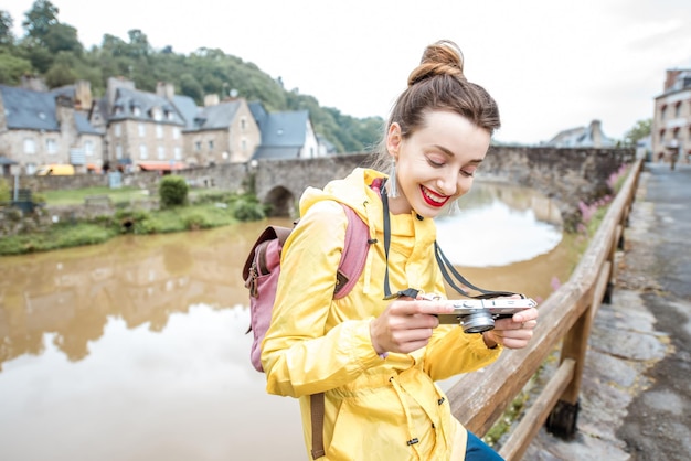 Młoda kobieta w żółtym płaszczu przeciwdeszczowym podróżująca z plecakiem i aparatem fotograficznym w wiosce Dinan w regionie Bretanii we Francji