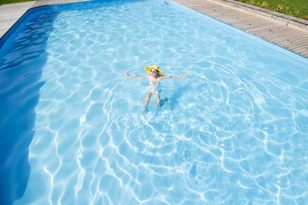 Młoda kobieta w żółtym sunhat pływanie w basenie z błękitną wodą. Widok ogólny z góry