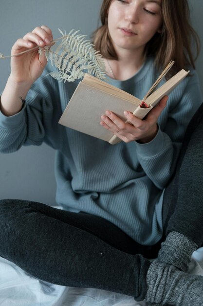 Zdjęcie młoda kobieta w zwykłych szarych ubraniach wyciąga suche liście z książki
