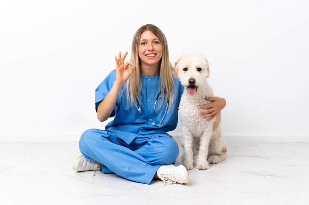 Młoda kobieta weterynarza z psem siedzi na podłodze, pokazując znak ok palcami