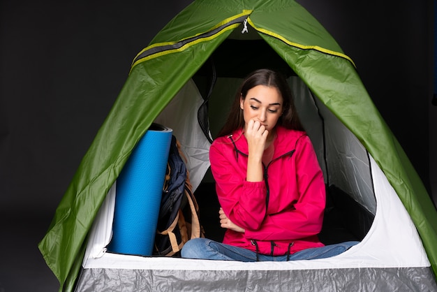 Zdjęcie młoda kobieta wewnątrz campingowego zielonego namiotu ma wątpliwości