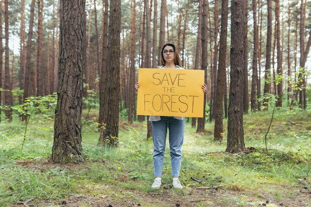 Zdjęcie młoda kobieta wolontariuszka w lesie pikietuje i trzyma plakat ratowania lasu