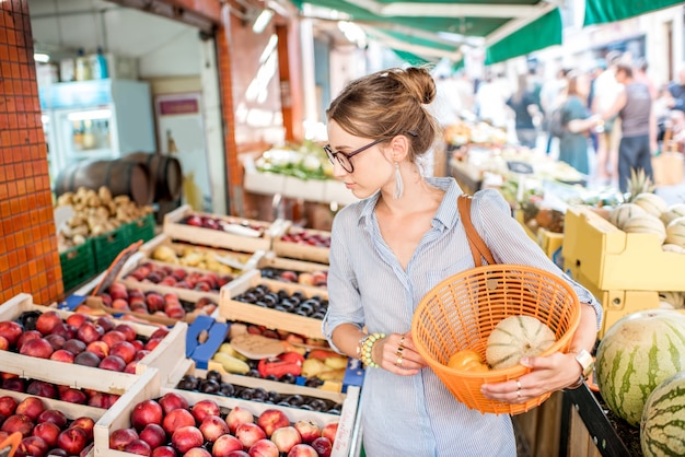 Młoda kobieta wybierająca świeżą brzoskwinię stojącą z koszem na targu spożywczym we Francji