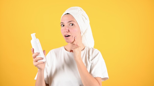 Młoda kobieta wyciera twarz pianką Kobieta trzyma pustą butelkę z dozownikiem na żółtym tle Koncepcja pielęgnacji skóry Zdjęcie wysokiej jakości