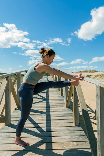 Młoda kobieta wykonująca pilatesyoga na drewnianym chodniku obok plaży