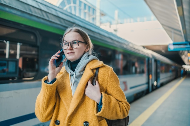 Młoda kobieta wykonuje telefon w roamingu, ma na sobie swobodną bluzę i żółty płaszcz, chętnie ekspresowo