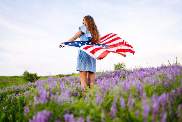 Młoda kobieta z amerykańską flagą USA na kwitnącej łące Dzień Niepodległości 4 lipca
