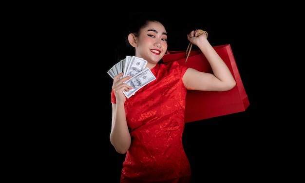 młoda kobieta z Azji w czerwonej sukience tradycyjny cheongsam trzyma torbę na zakupy i banknot 100 USD