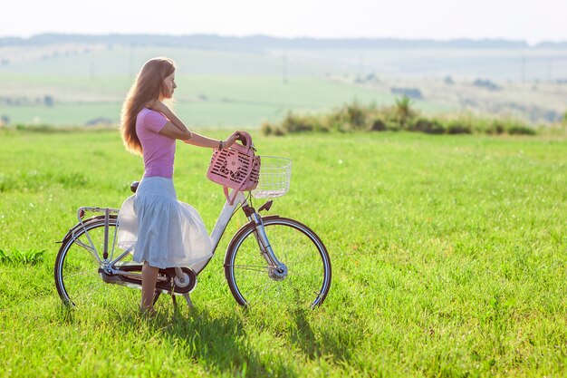 Młoda kobieta z bicyklem na zieleni polu na słonecznym dniu