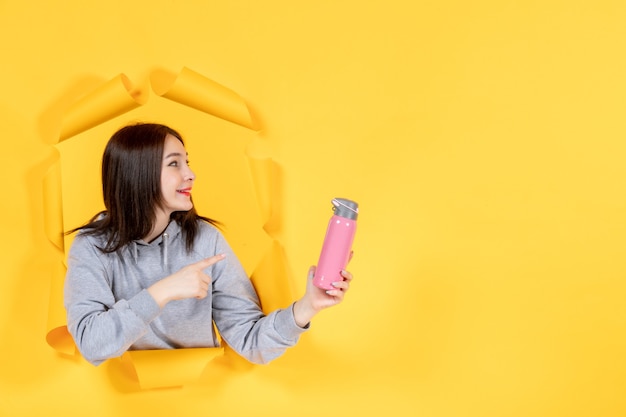 młoda kobieta z butelką wody na żółtym tle papieru sportowiec siłownia fit