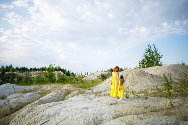Młoda kobieta z córką w żółtej sukience w pobliżu jeziora z lazurową wodą i zielonymi drzewami. Koncepcja szczęśliwego związku rodzinnego