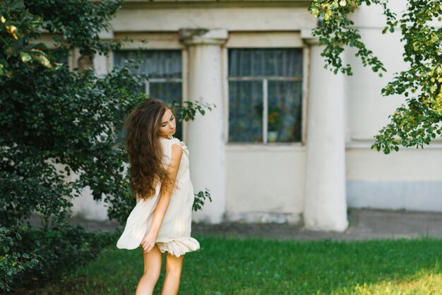 Młoda kobieta z długimi włosami biega latem przez trawę w miejskim parku, jej włosy trzepoczą