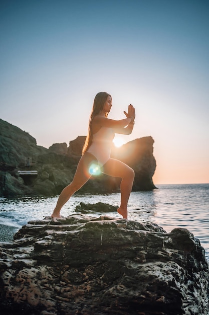 Młoda kobieta z długimi włosami w białym stroju kąpielowym i bransoletkach w stylu boho, ćwicząca na świeżym powietrzu na macie do jogi