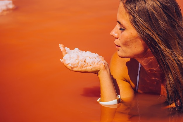 Młoda kobieta z długimi włosami w różowym słonym jeziorze z kryształkami soli niezwykle słonym różowym jeziorem