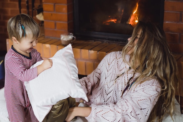 młoda kobieta z dzieckiem. Mama i syn żartują, bawią się przy kominku.