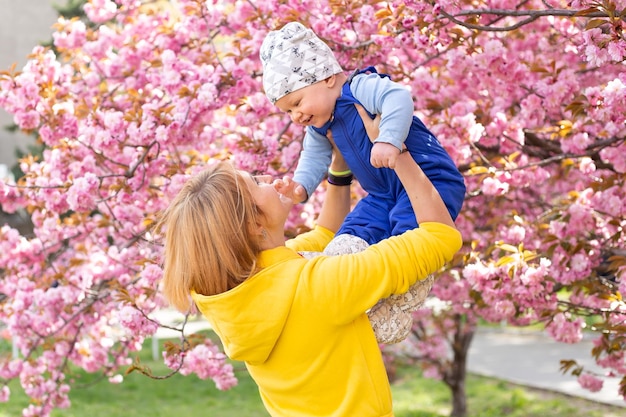 Młoda kobieta z dzieckiem w ramionach szczęśliwa sakura kwitnąca wiosną Park Radość macierzyństwa i rozwoju dziecka Kwitnąca wiśnia późną wiosną