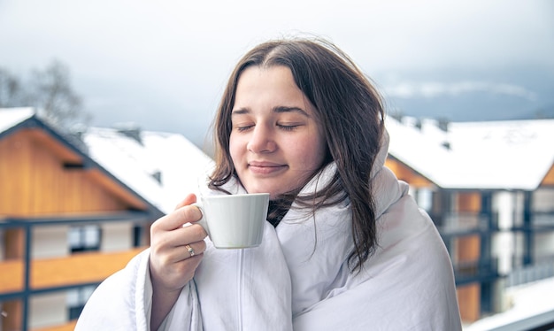 Młoda kobieta z filiżanką kawy na balkonie zimą w górach